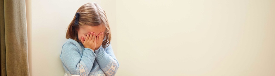 Verdrietig meisje met knuffel in de hoek van de kamer